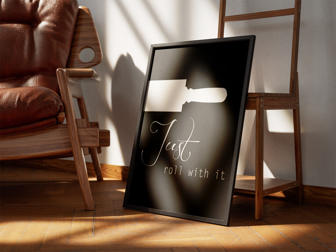 Minimalist chalkboard art with a white rolling pin and the script text 'Just roll with it' on a dark background.