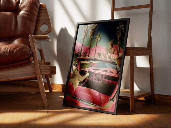 A white cat in a vintage pink convertible drives past tall palm trees and vibrant pink mountains under a blue sky.